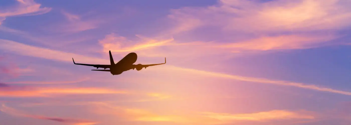 Silhouette of plane flying against a pink and purple dawn sky